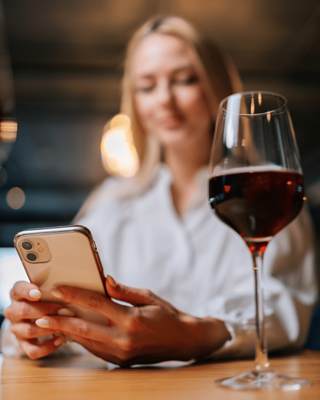 A girl on her phone with a glass of red wine